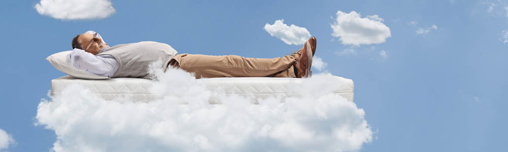 Older man lying back with his hands behind his head, floating in the clouds. Bright blue sky and white clouds floating around him.